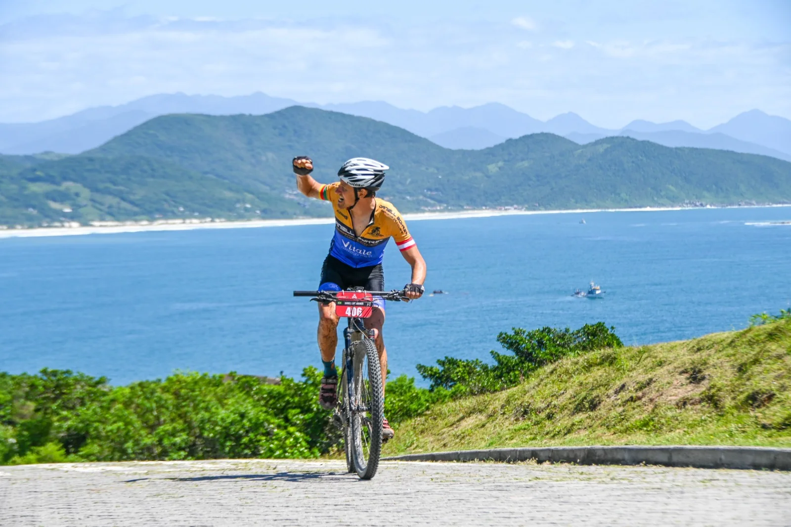 Ciclista comemora durante uma subida com o litoral ao fundo